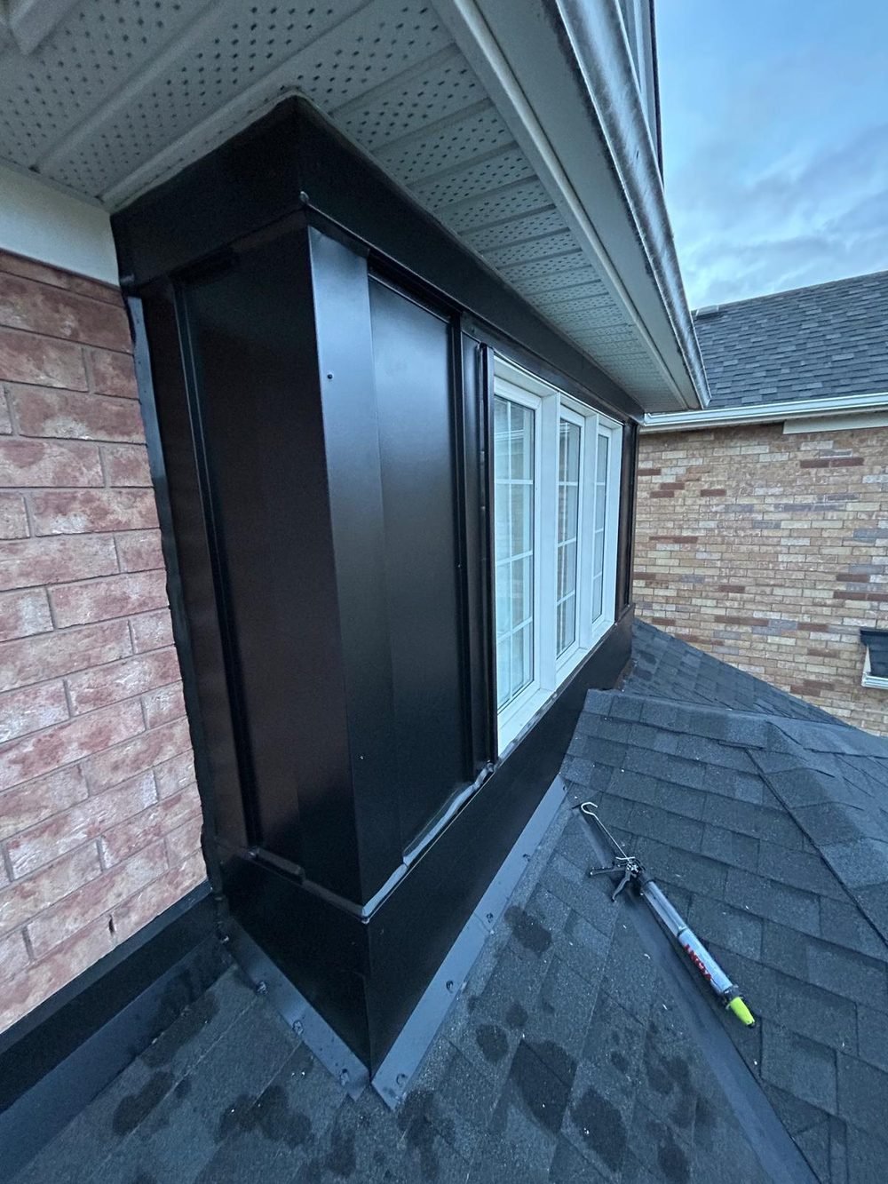 Corner of a black aluminum capped window bay above a shingled roof