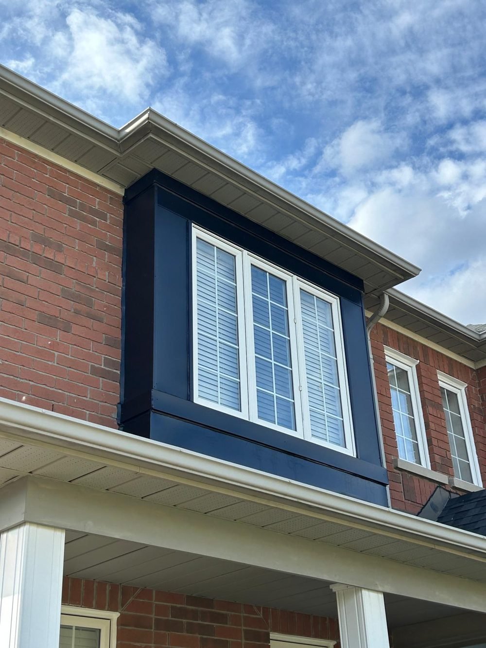 Dark capped dormer window on a brick home under a blue sky