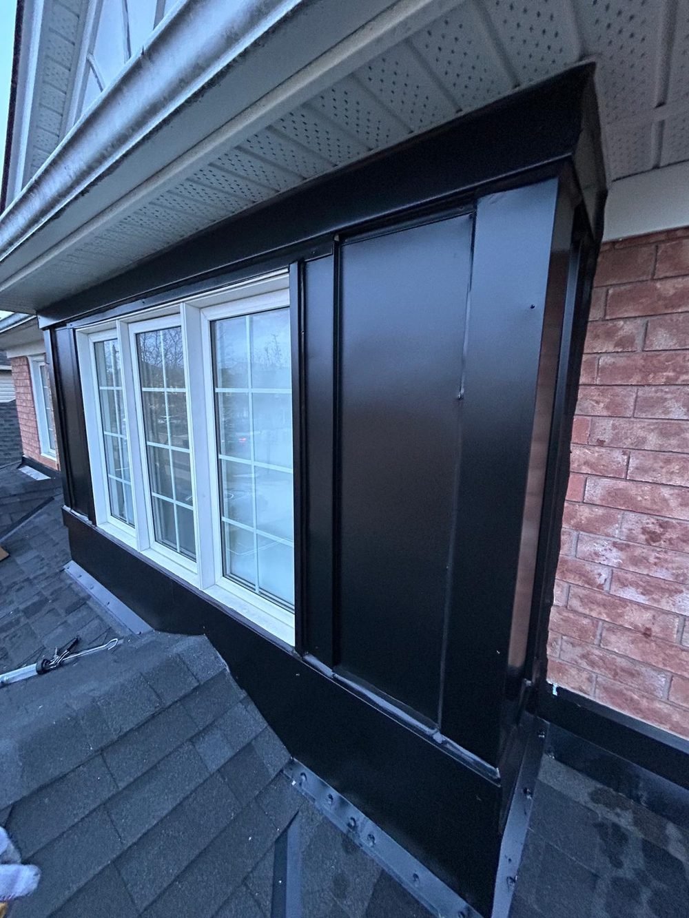 Window with black aluminum capping and caulking on a brick home