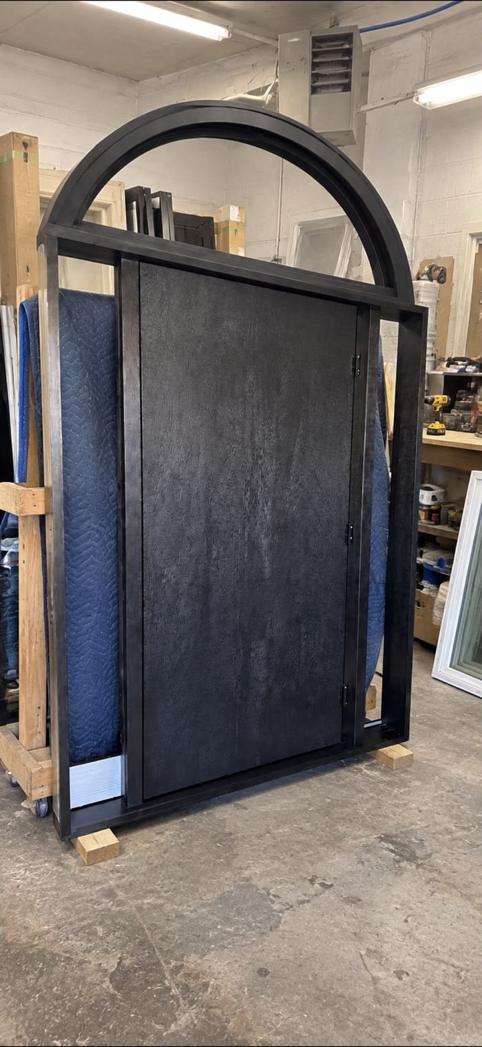 Arched black front door frame with a dark slab door in a workshop