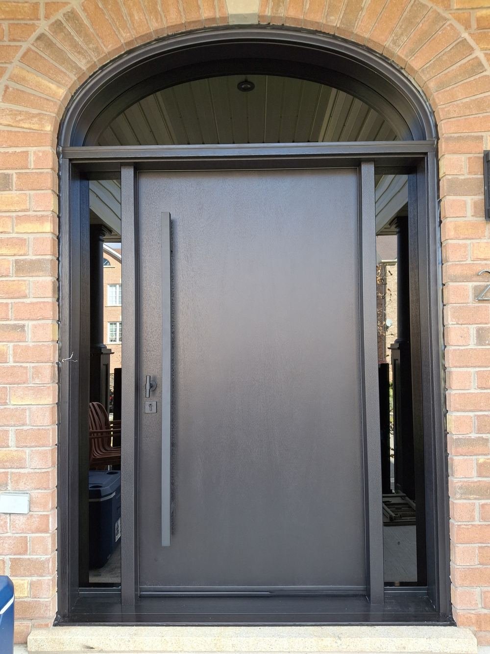 Dark pivot front door with sidelites and arched transom in a brick entry