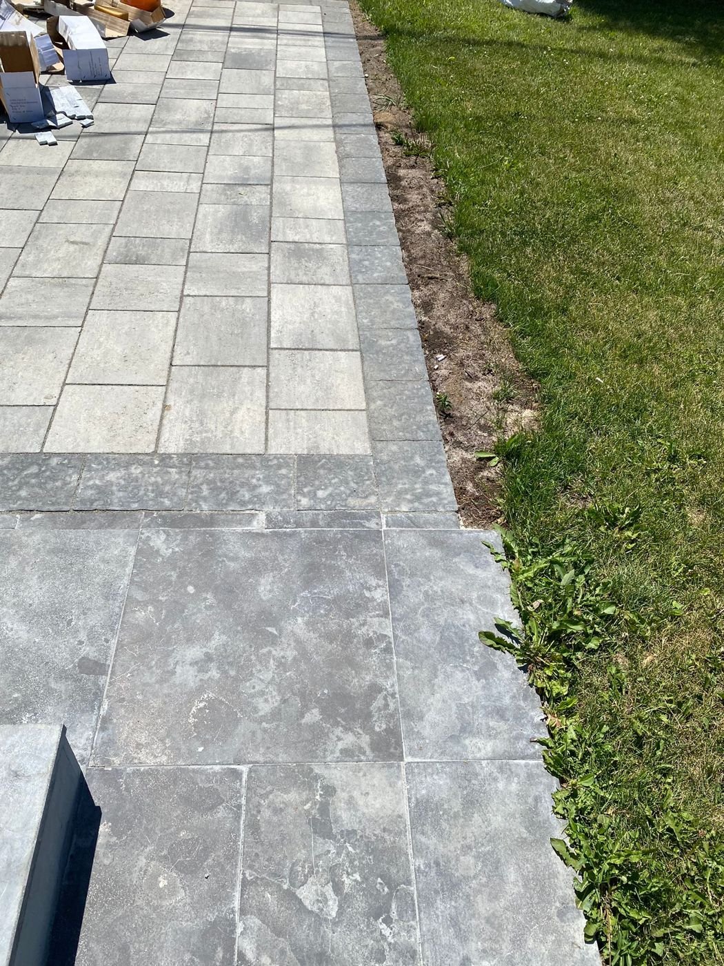 Grey interlocking walkway with a dark border meeting a stone landing beside the lawn