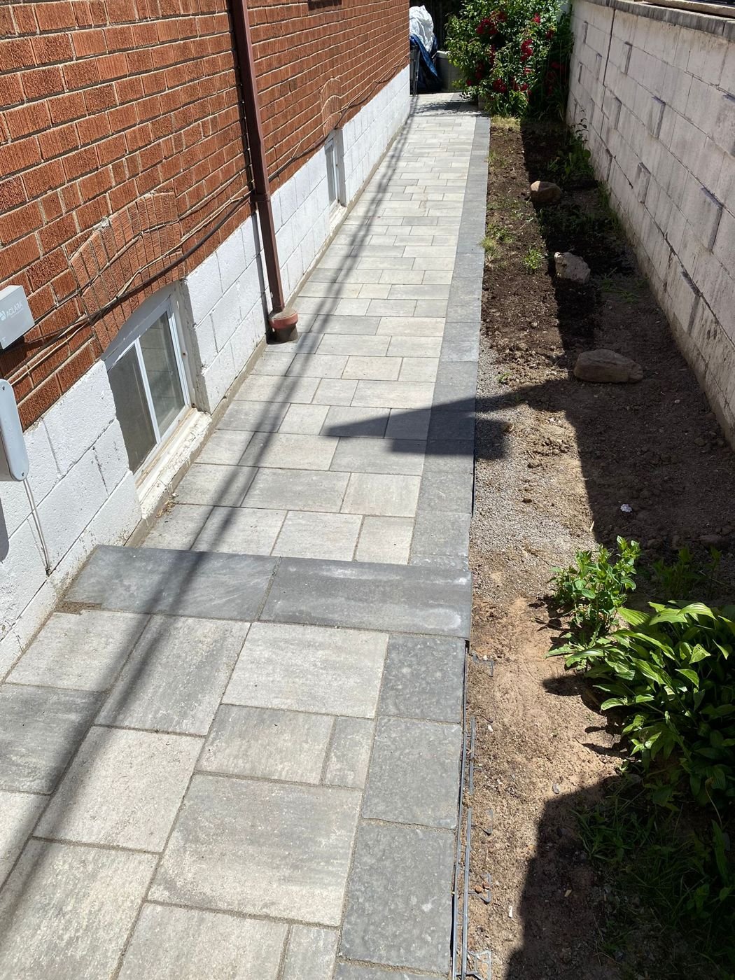 Side walkway of large format interlocking pavers with a dark border along a brick home