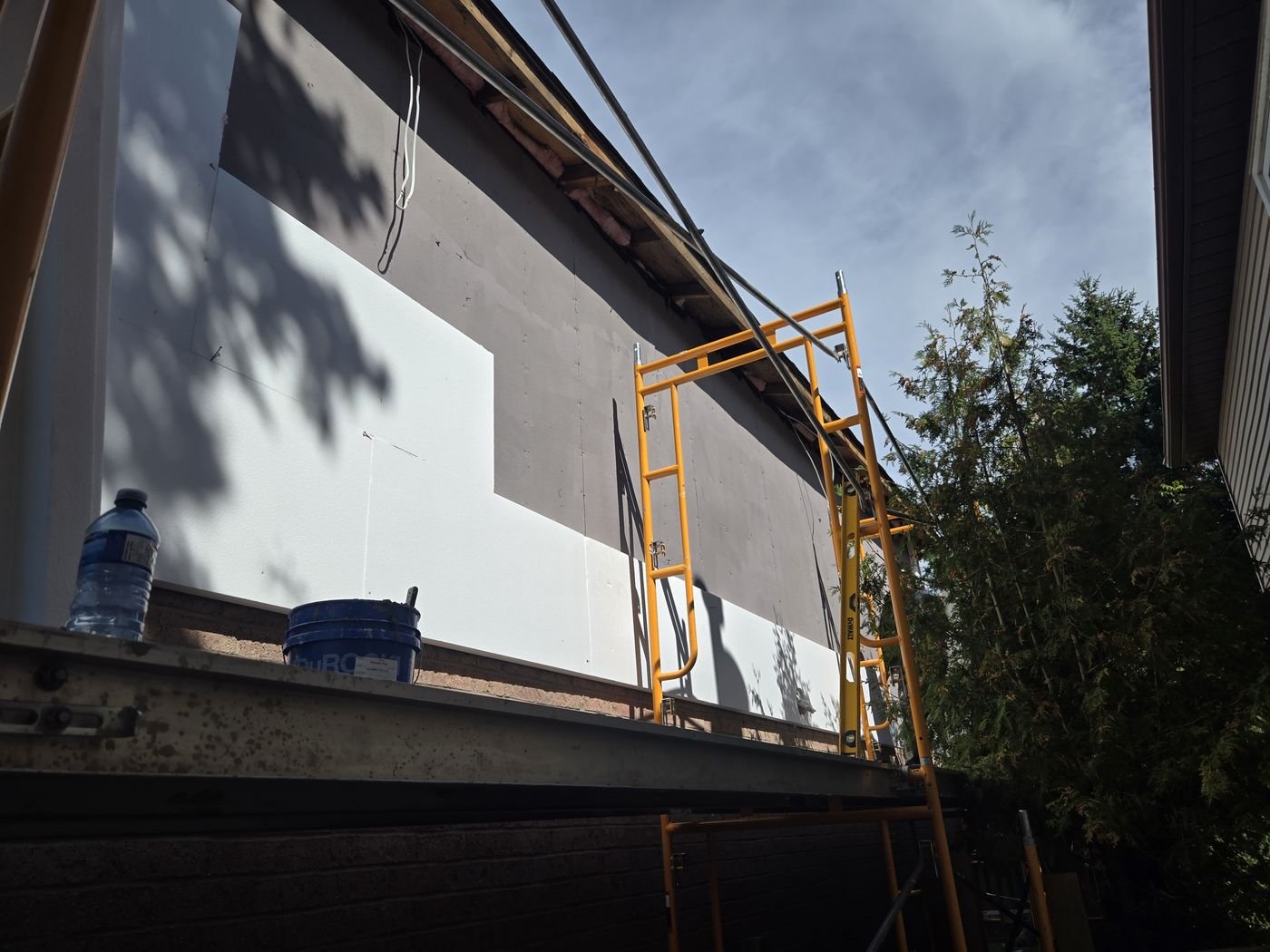 Stucco work in progress on an exterior wall above brick with scaffolding
