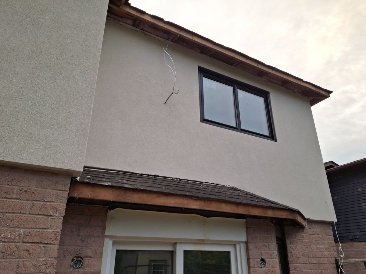 Finished stucco wall with new black windows above brick