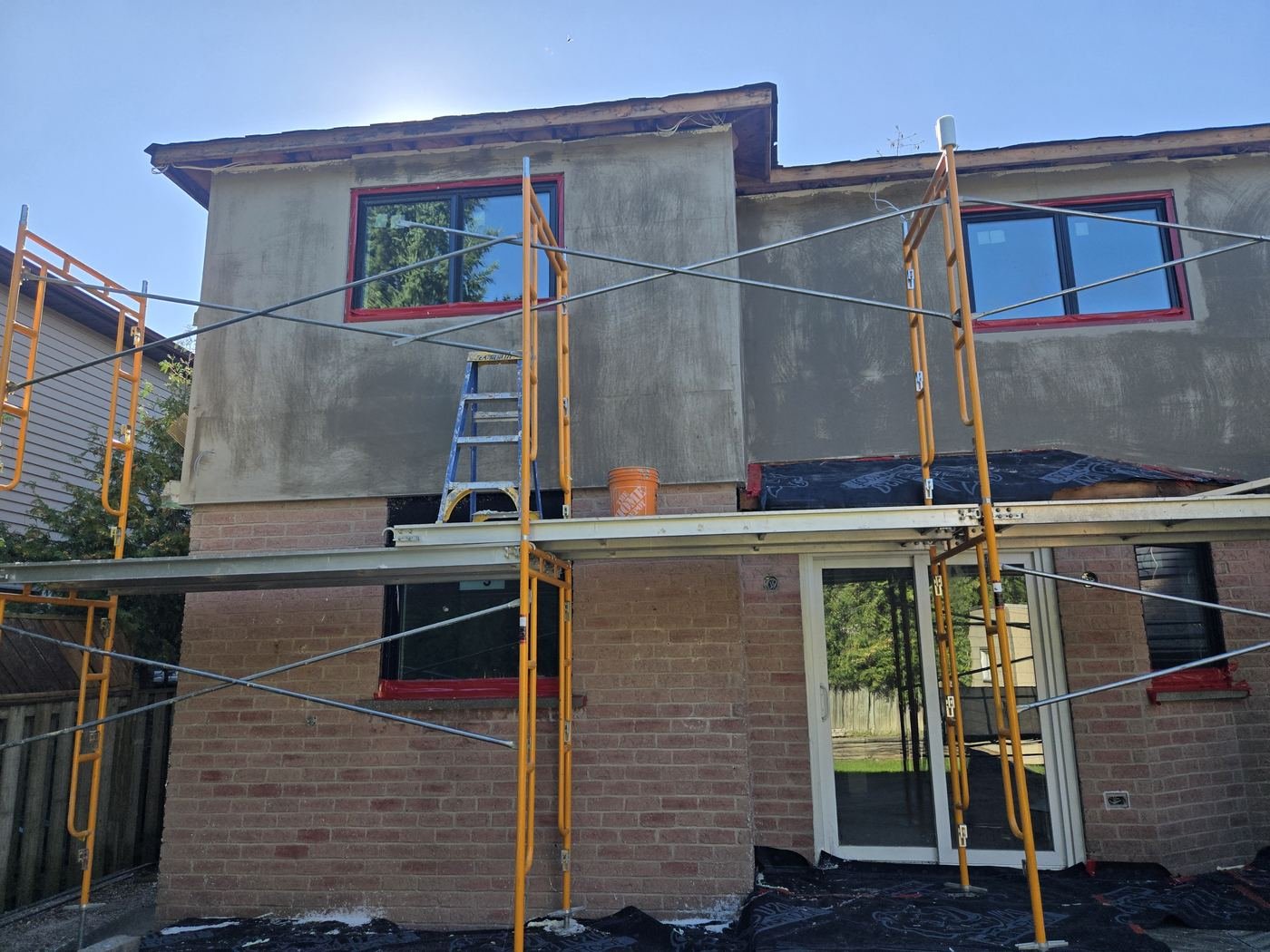 Stucco base coat on the rear of a home with scaffolding and new windows